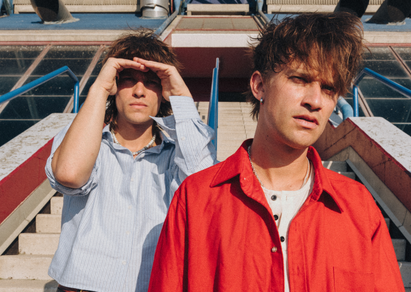 Two people one with a button down shirt pn and another with a red back standing on steps.x